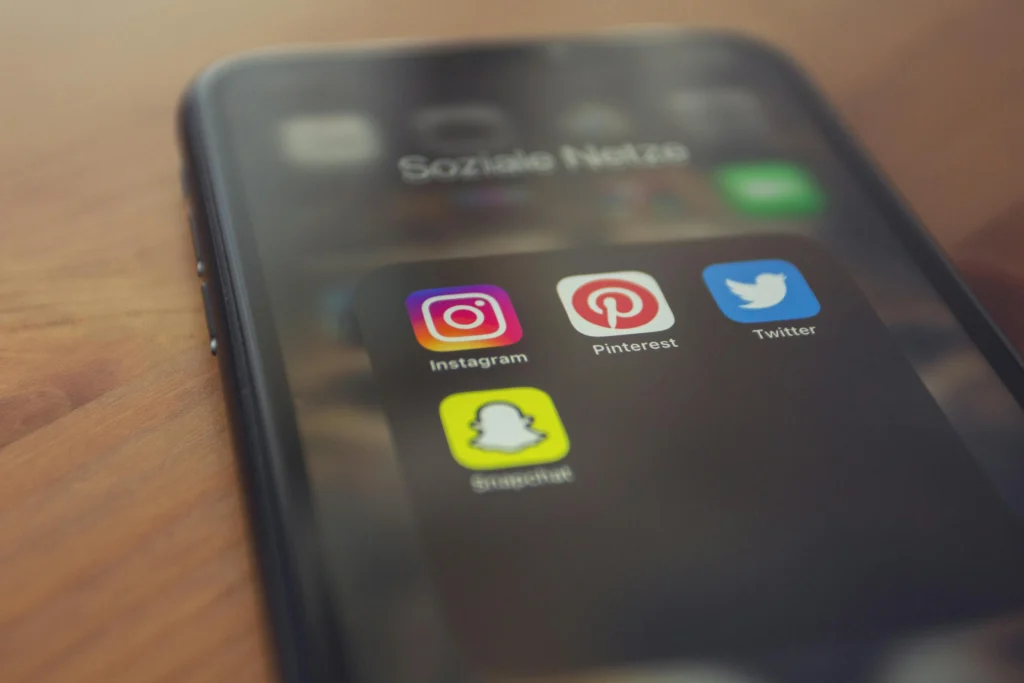 Close-up of a smartphone screen showing social media app icons: Instagram, Pinterest, Twitter, and Snapchat on a dark background.
